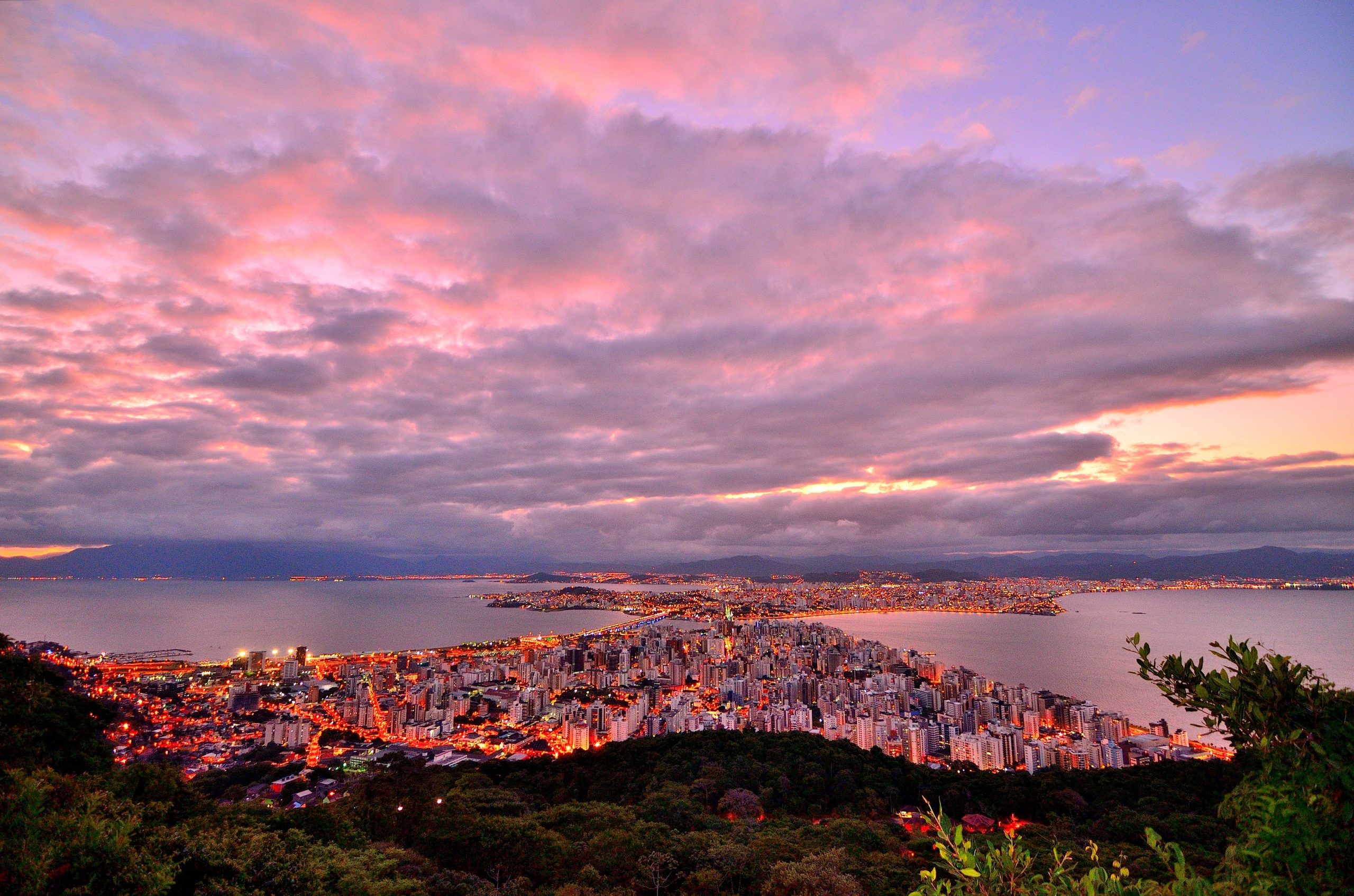 Vista do Centro de Florianópolis ao entardecer, com a cidade entre o mar e as colinas