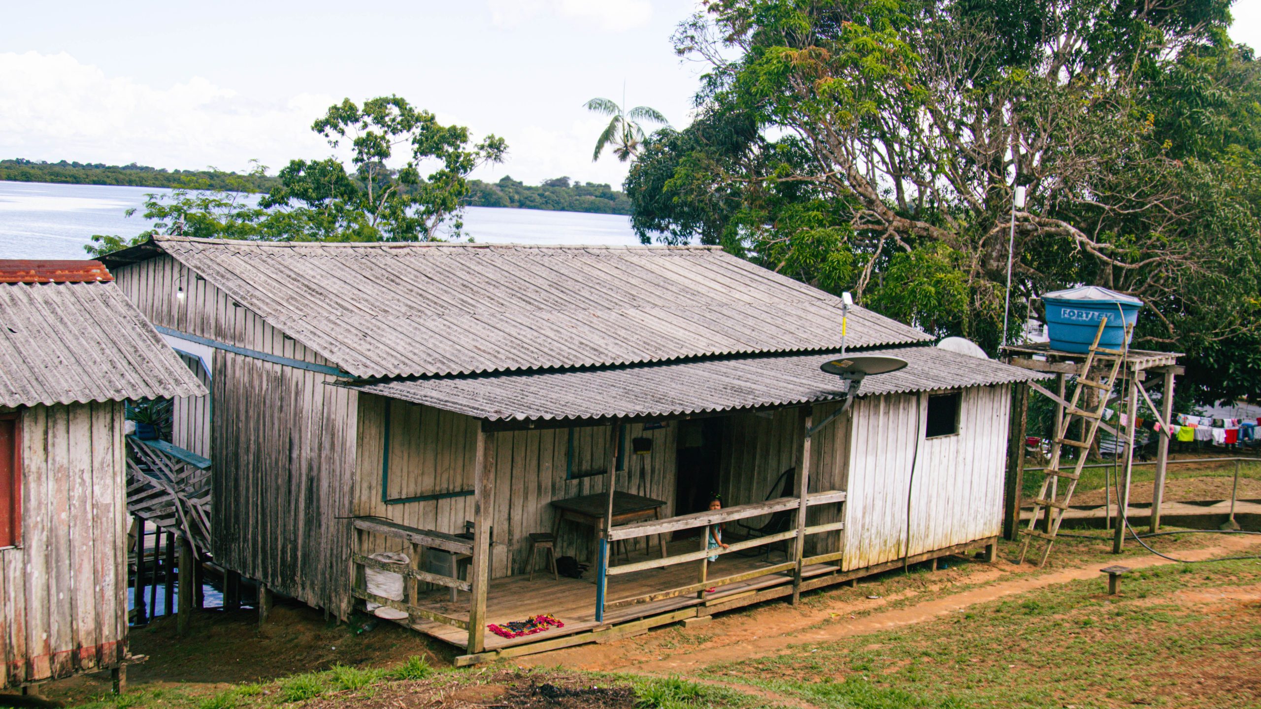 Casa ribeirinha de madeira sobre palafitas à beira de um rio da bacia amazônica, cercada por vegetação densa e água calma, em Manaus, no Amazonas
